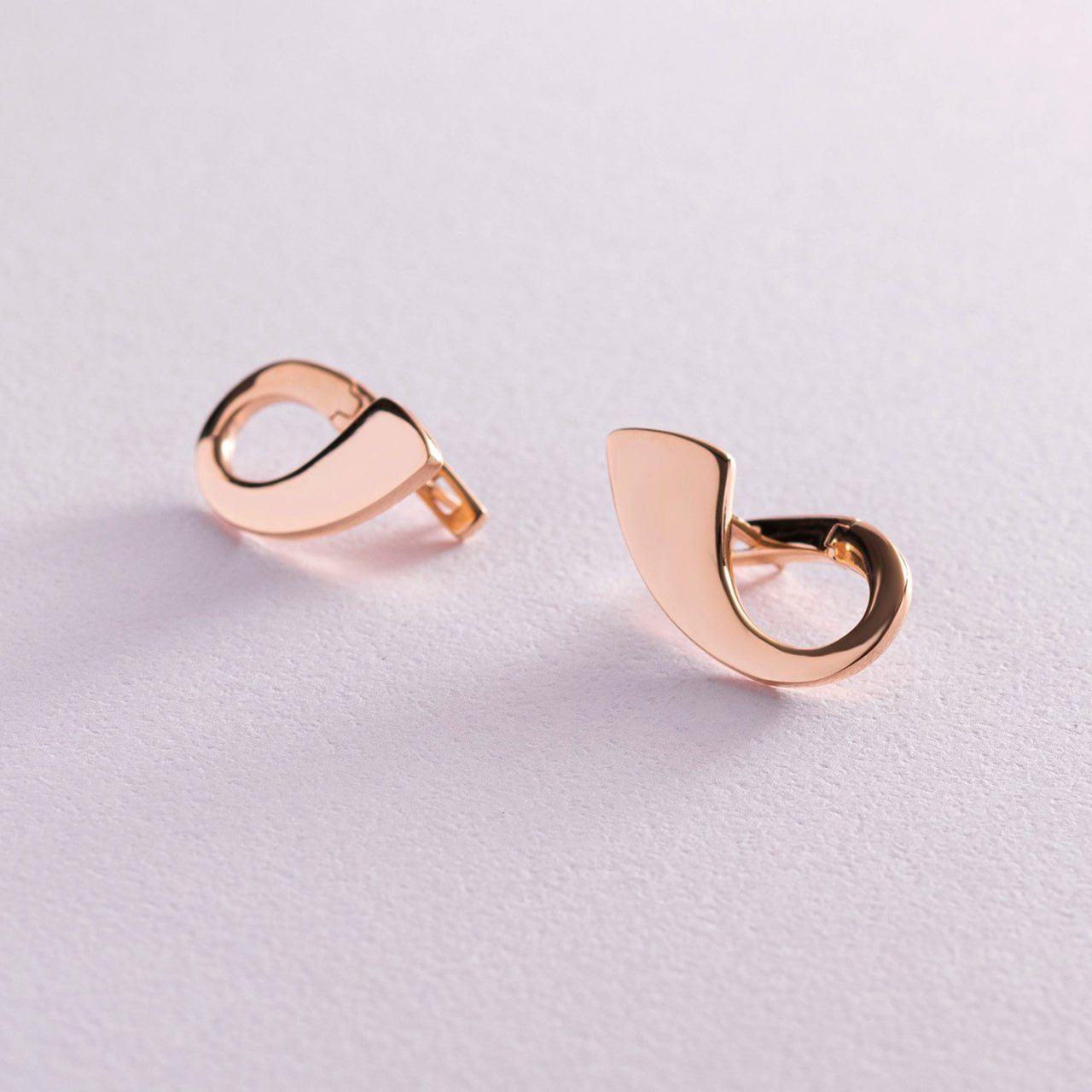 A pair of minimalist, open crescent-shaped hoop earrings in polished rose gold, displayed on a clean, light pink textured surface-Lightweight and comfortable for everyday wear earrings