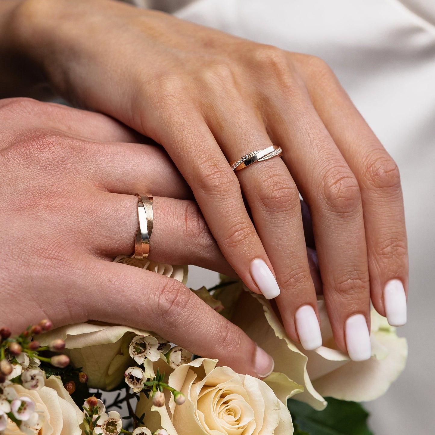 A close-up of two hands resting on cream roses, with one hand wearing a silver band and the other wearing a gold band-- 14k solid gold- combination of matte and polished finish- 5.5 mm wide band
