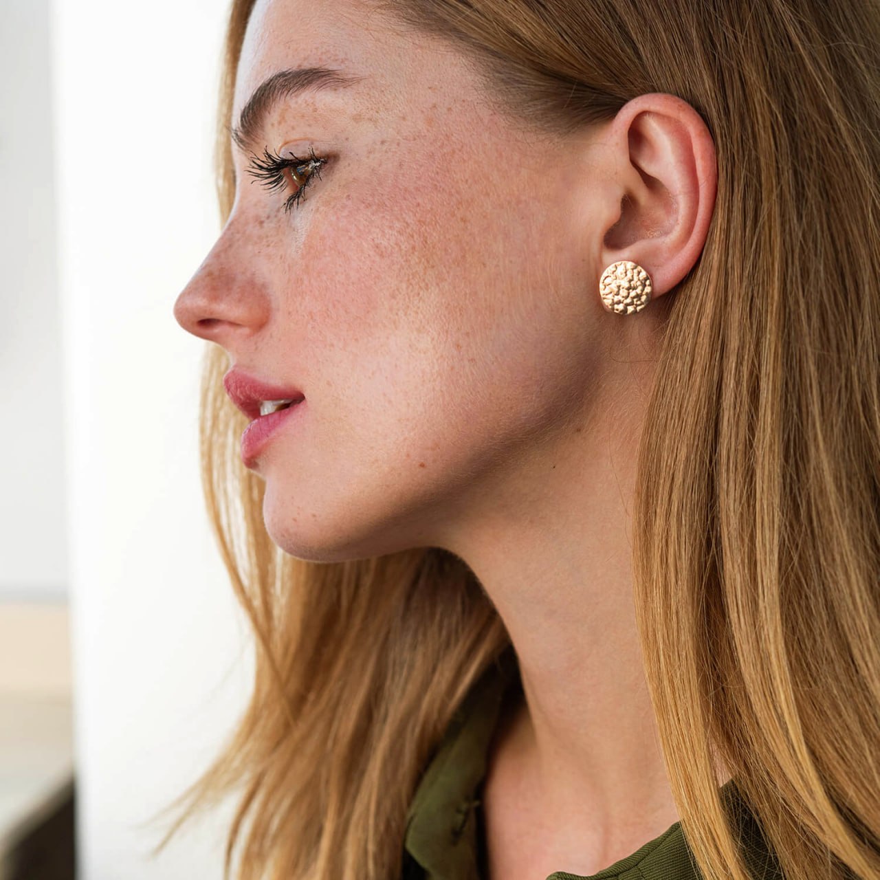 A close-up side profile of a woman with freckles wearing a textured, round gold stud earring-statement stud earrings-circle earrings
-everyday gold earrings