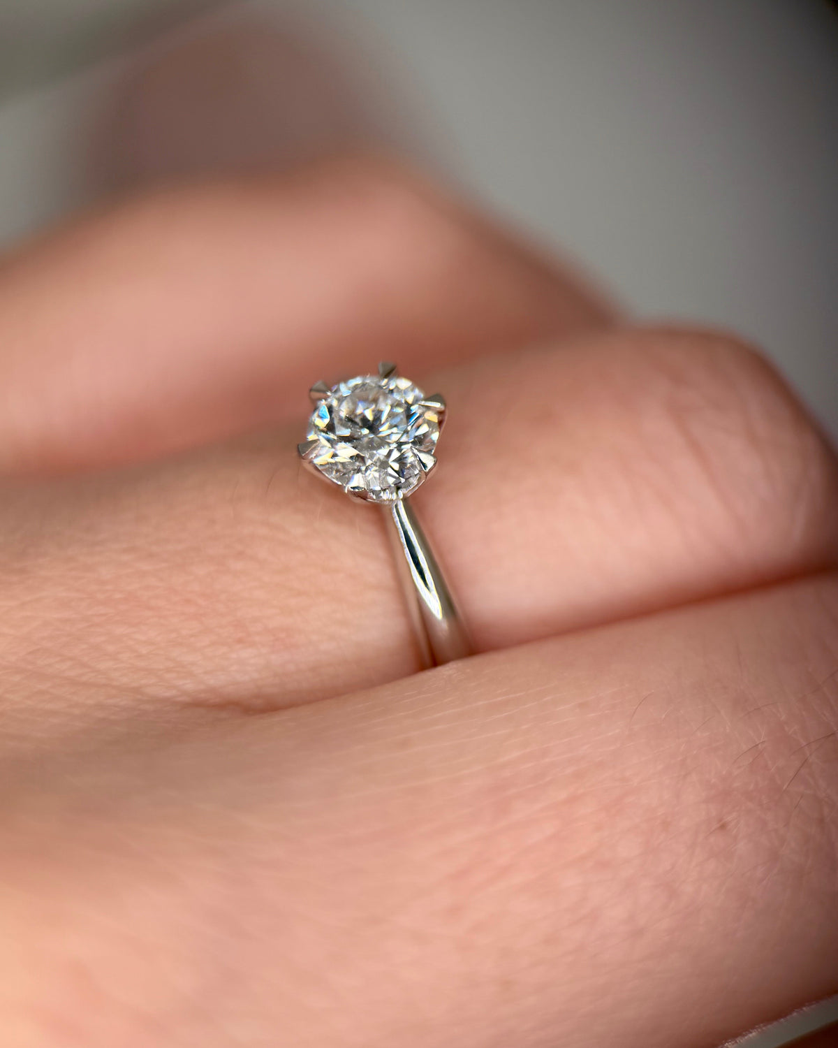 A close-up shot of a classic solitaire diamond engagement ring on a silver band, worn on a person's ring finger-lab grown diamond-promise ring for her-minimalist engagement ring