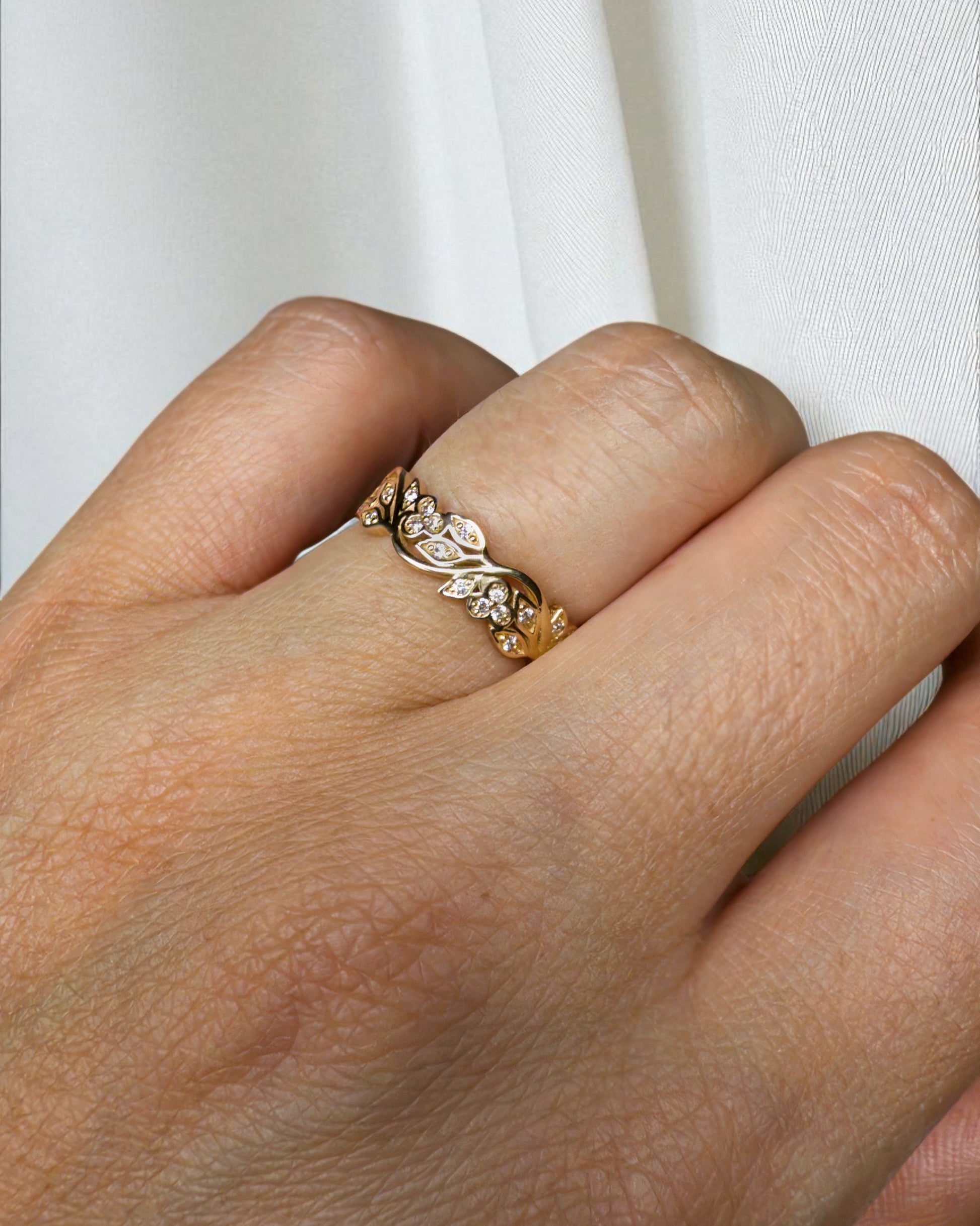 Gold ring with floral design on a person's finger -full circle of blossoms and shimmering stones