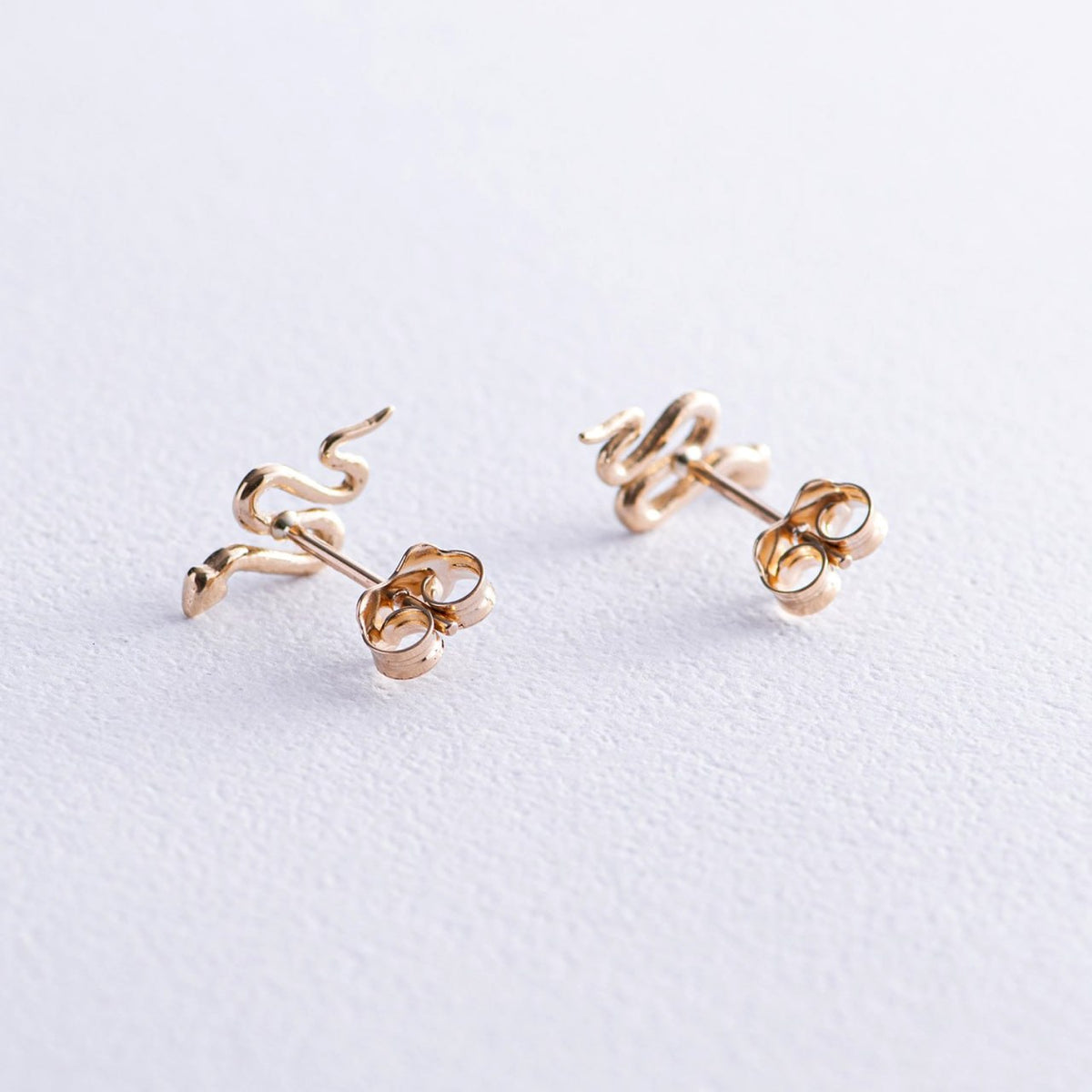 A pair of gold post earrings with a twisted snake design, shown from the back on a textured white surface-everyday earrings
gift for her
no stone earrings