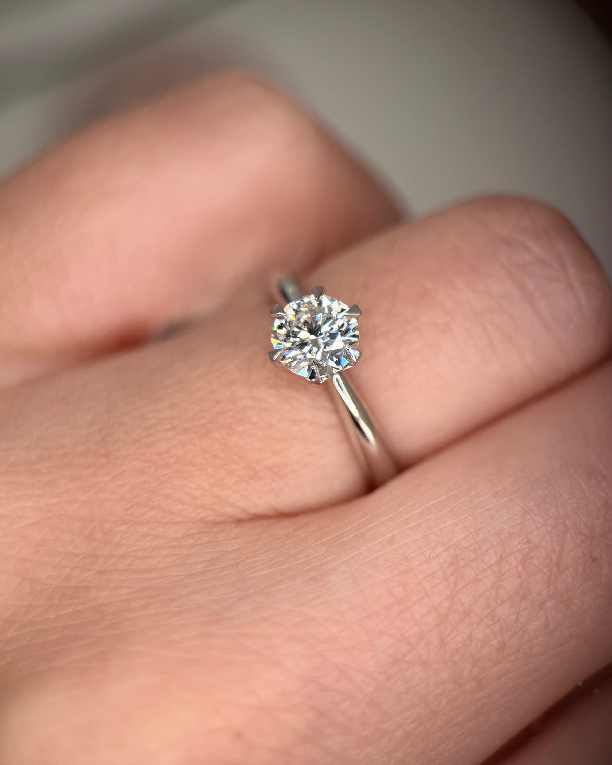A close-up shot of a classic solitaire engagement ring with a round brilliant-cut diamond on a silver band, worn on a person's finger-Band: Polished plain band