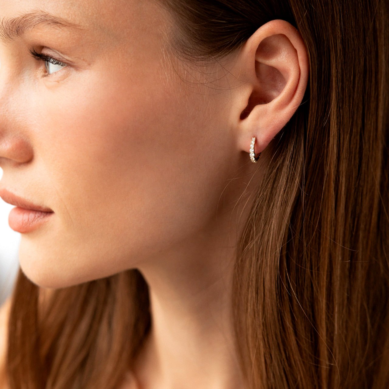 A close-up side profile of a woman wearing a small silver crescent-shaped hoop earring set with tiny clear stones-sparkle hoop earrings-gift for her-delicate gold hoops