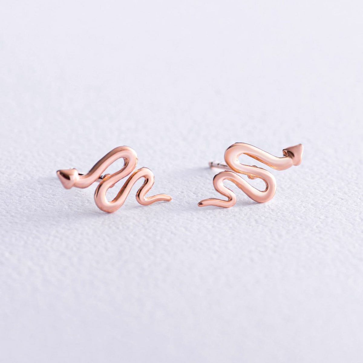 A pair of rose gold snake stud earrings on a textured light gray background-minimalist gold studs
snake jewelry
solid gold earrings