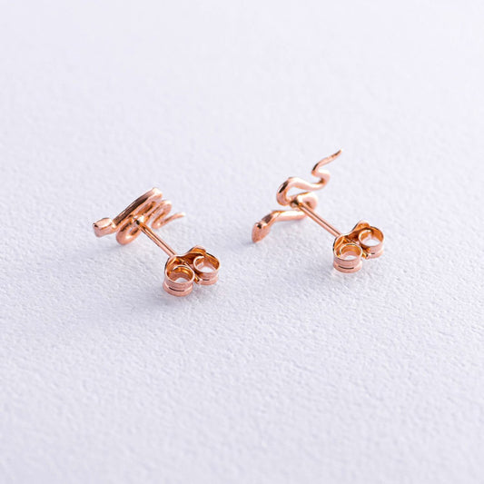 A pair of rose gold stud earrings with a unique coiled snake design, displayed on a textured white surface-snake earrings
gold stud earrings
14k gold earrings