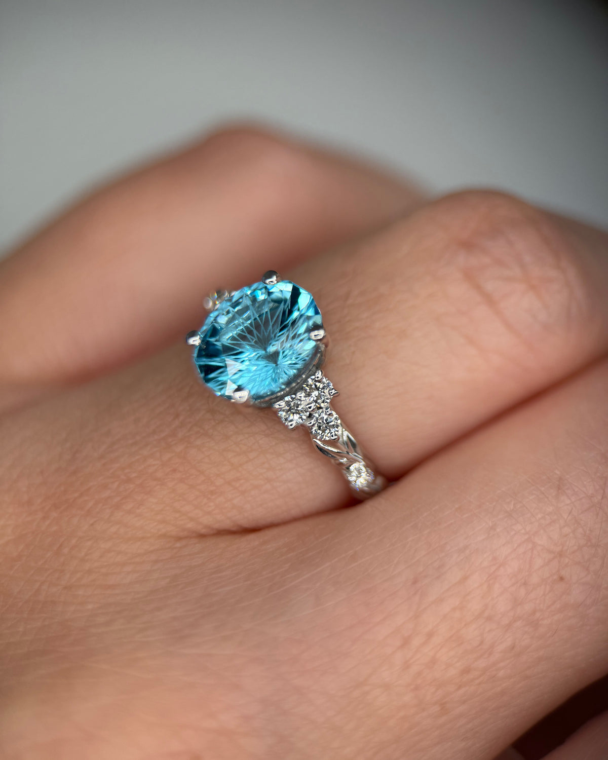 A close-up of a hand wearing a silver ring with a large oval-cut light blue gemstone and small accent stones on the band-statement gemstone ring
vine leaf ring-blue stone engagement ring