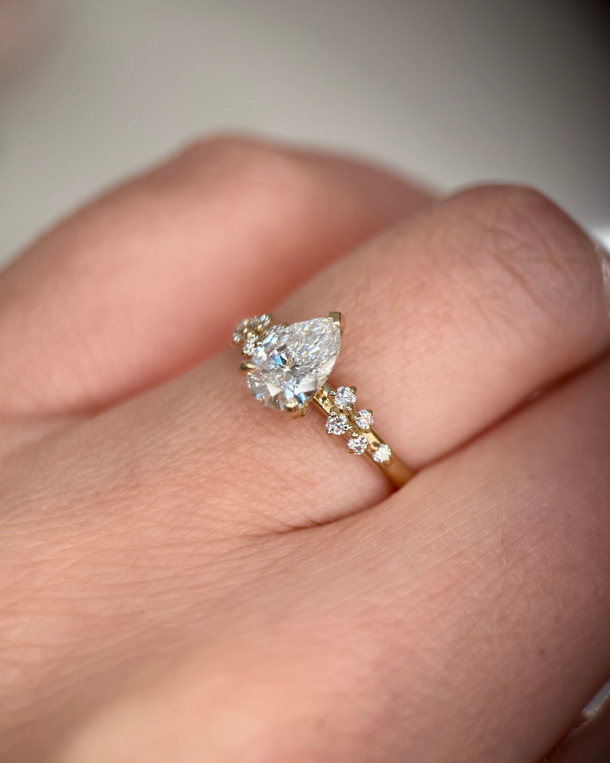 A close-up of a hand wearing a yellow gold ring featuring a pear-cut clear center stone and smaller round stones along the band-Metal: 14k Yellow Gold (585), solid