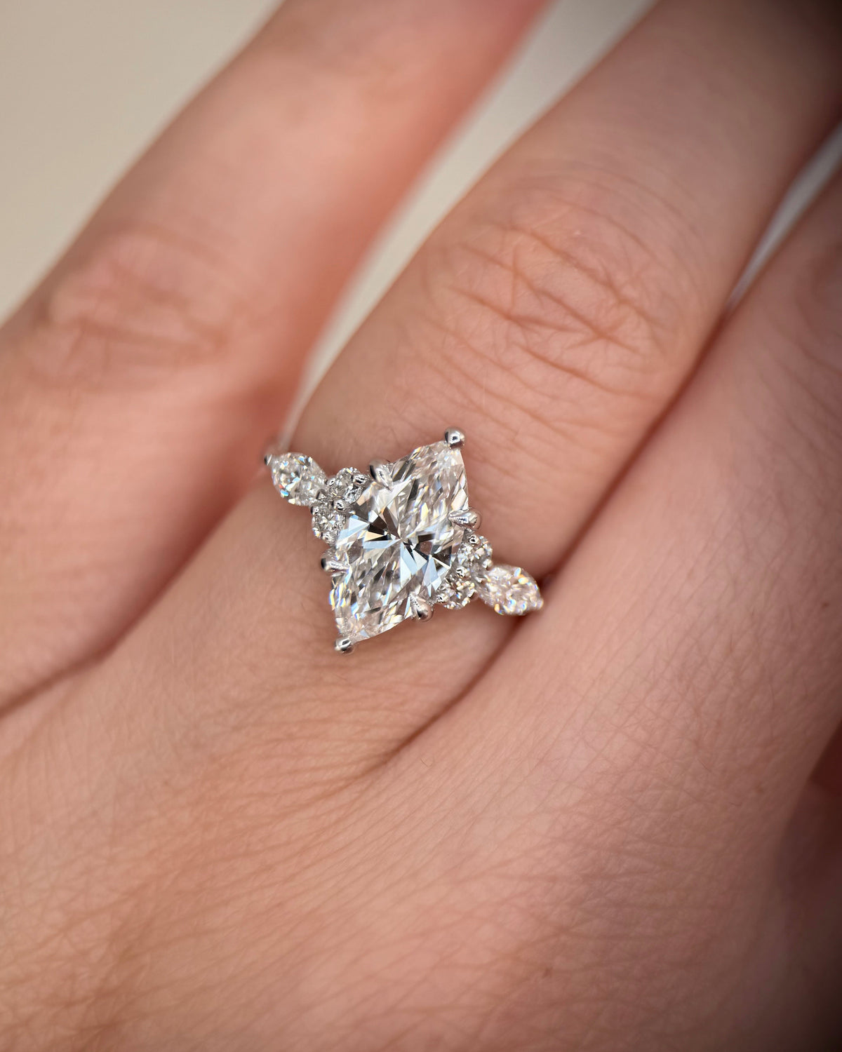 A close-up of a hand wearing a silver-toned ring with a large clear marquise-cut center stone and smaller side stones-marquise engagement ring-cluster engagement ring-white gold engagement ring-art deco engagement ring